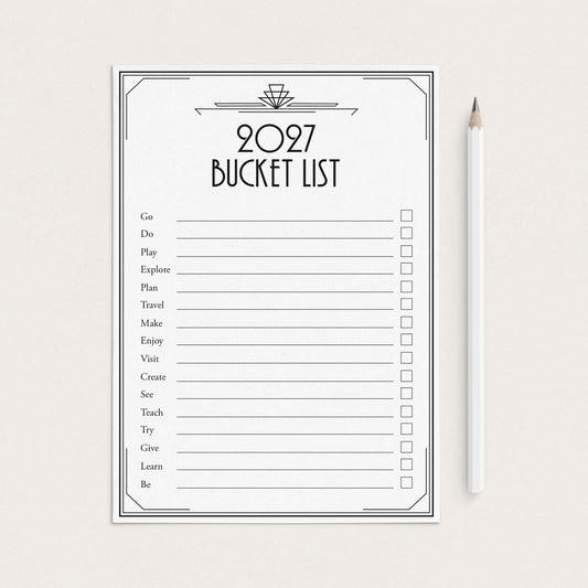 A 2027 bucket list printable sheet with black text and checkboxes on a white background, styled flat-lay next to a white pencil on a light beige surface.