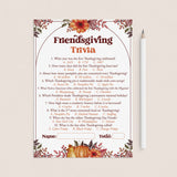 A Thanksgiving trivia game card with floral fall border illustrations, shown on a light beige background next to a white pencil. The card features a central arch with the title 'Friendsgiving Trivia' and ten multiple-choice questions with answer options listed below.
